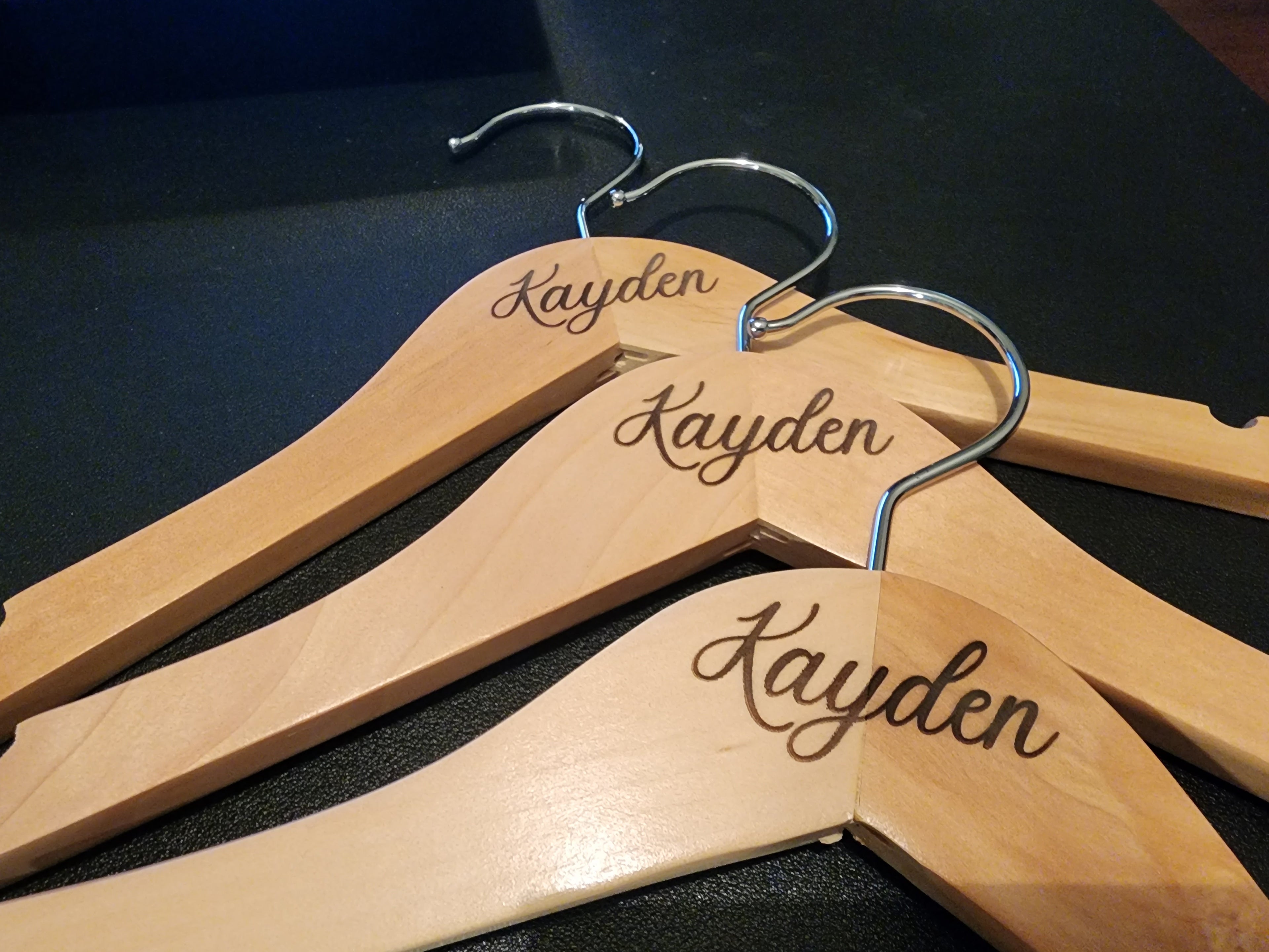 Three wooden hangers with 'Kayden' engraved on them, placed on a dark surface.