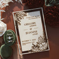 Wedding invitation card with floral design on a brown background with flowers and rings.