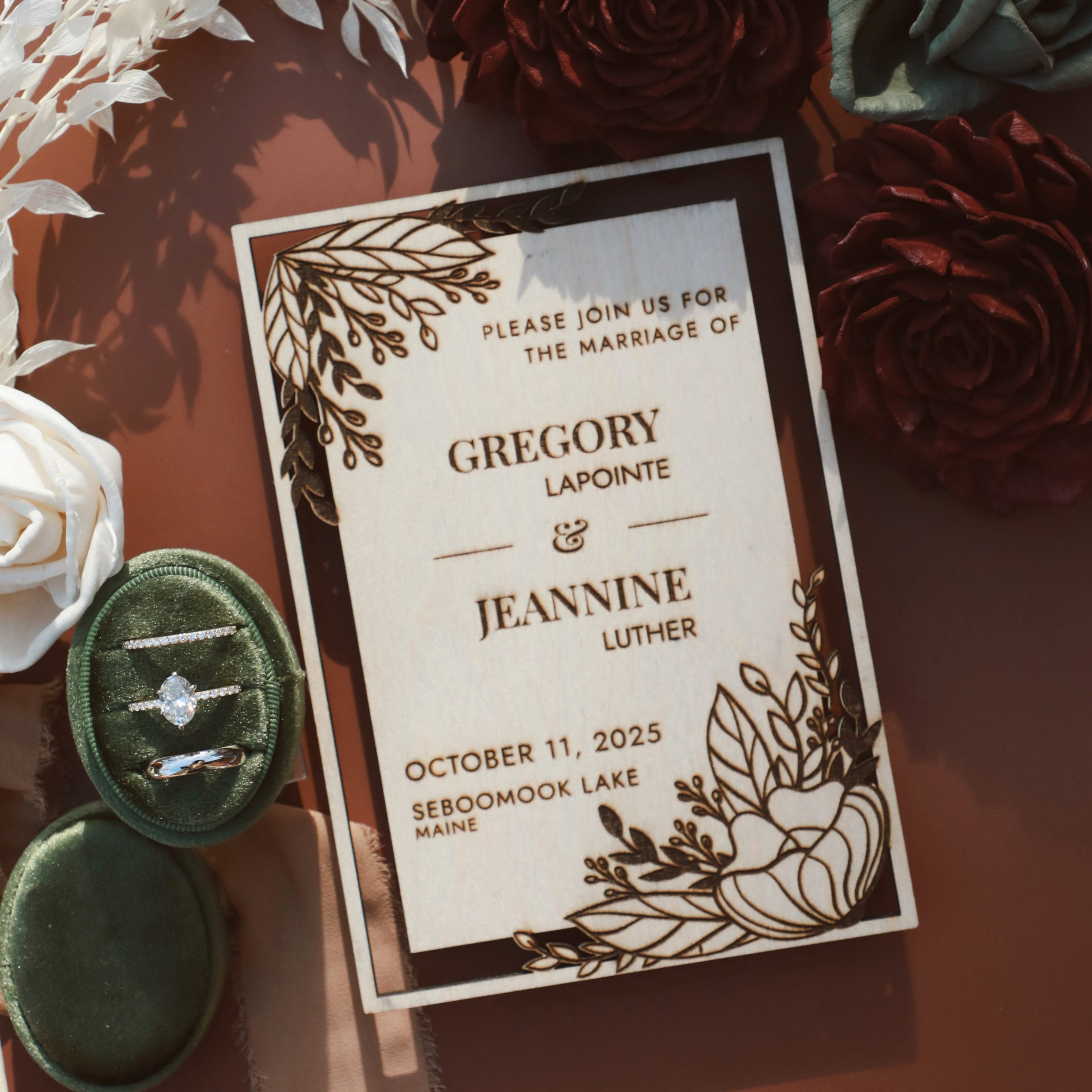 Wedding invitation card with floral design on a brown background with flowers and rings.
