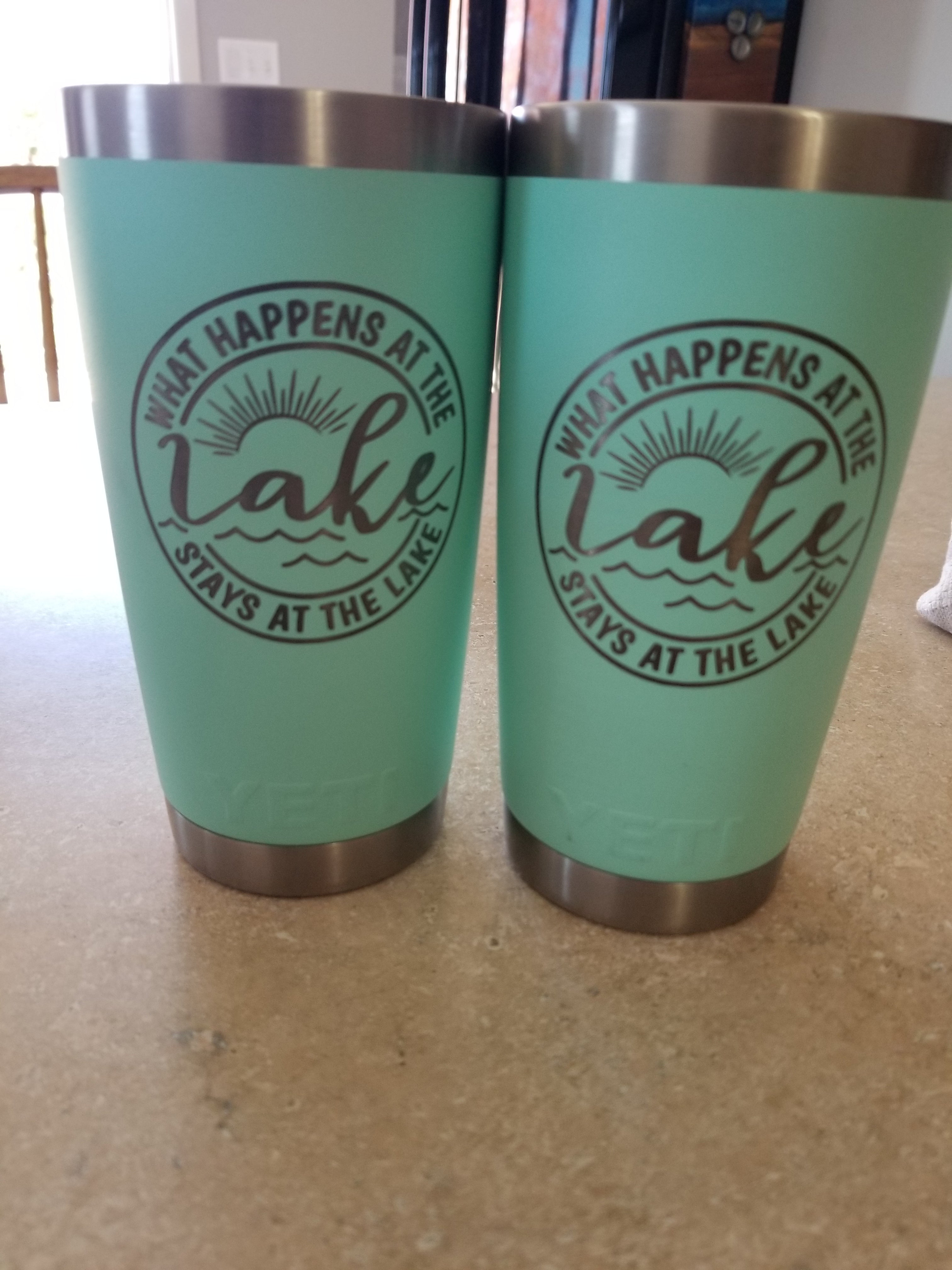 Two green tumblers with a logo and text on a beige surface