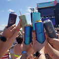 People holding up colorful tumblers at a concert with a stage and 'Ocean Conservation' sign in the background.